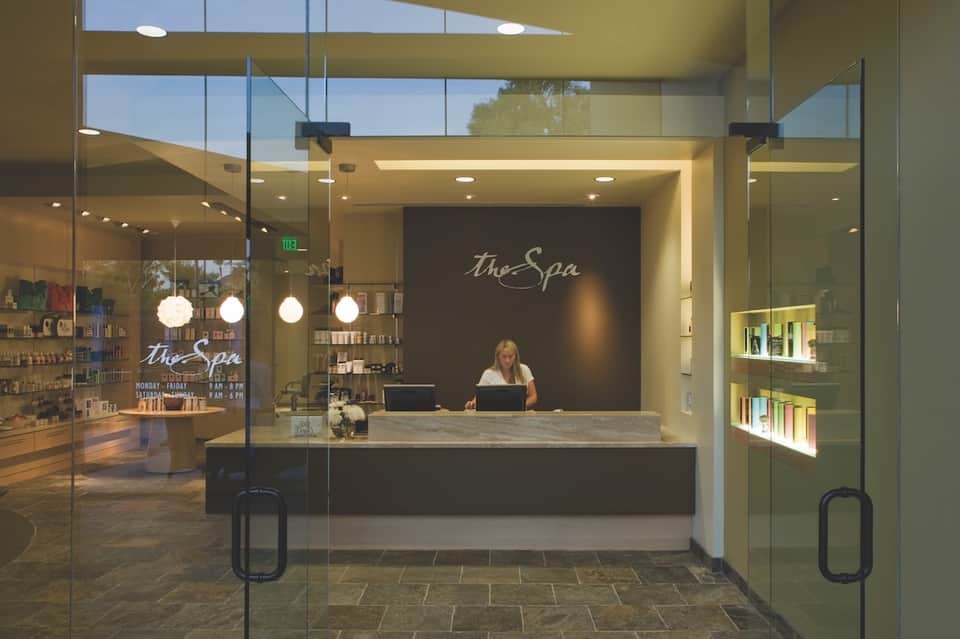 Modern spa reception desk with glass doors, pendant lighting, and retail shelving