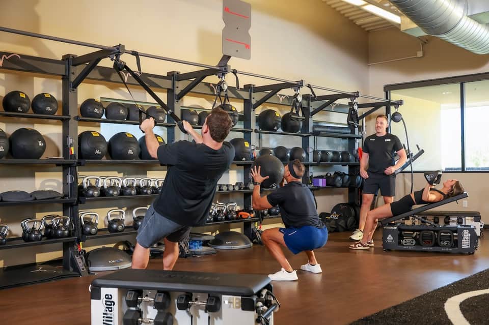 Group fitness class in motion with suspended equipment, medicine balls, and instructor in gym