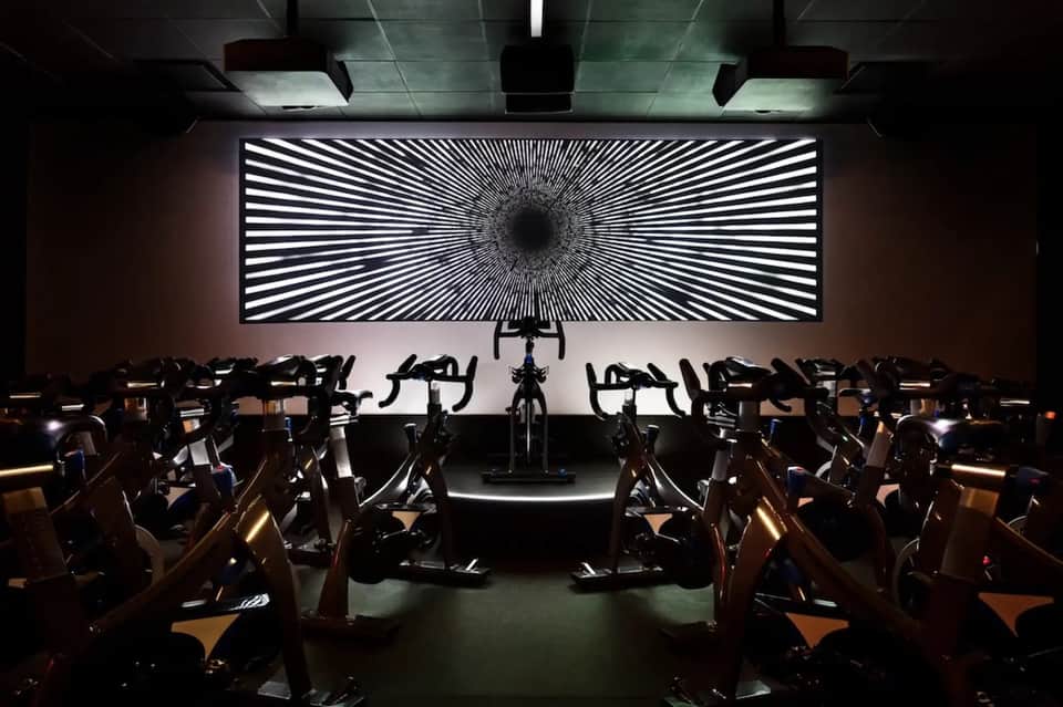 Indoor cycling studio with stationary bikes arranged facing large screen display