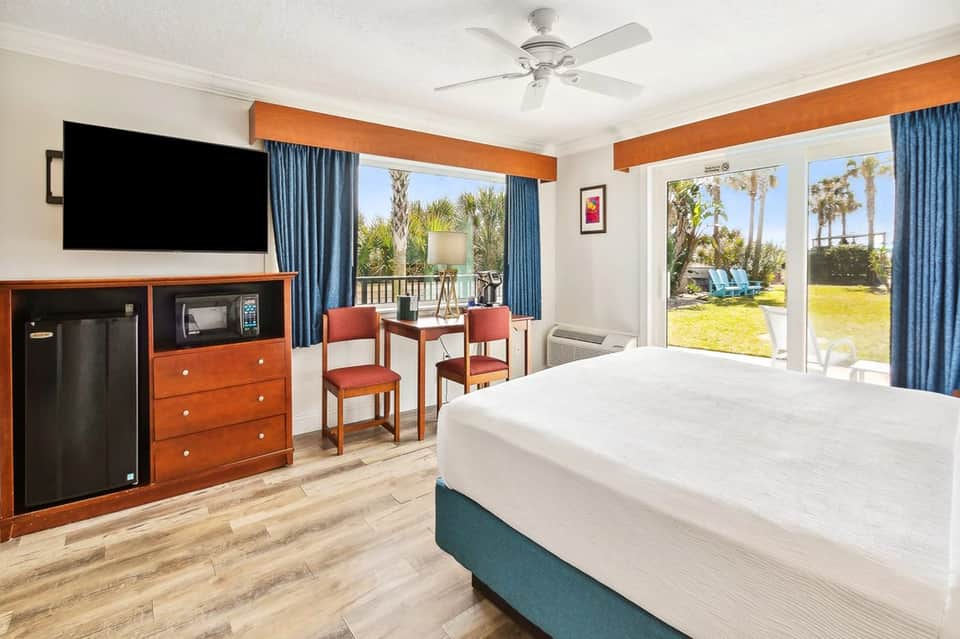 Hotel bedroom with ocean view balcony, flat-screen TV, and coastal decor