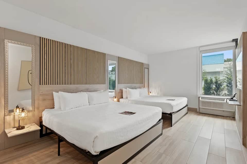Modern hotel room with two queen beds, wooden accent wall, and contemporary furnishings