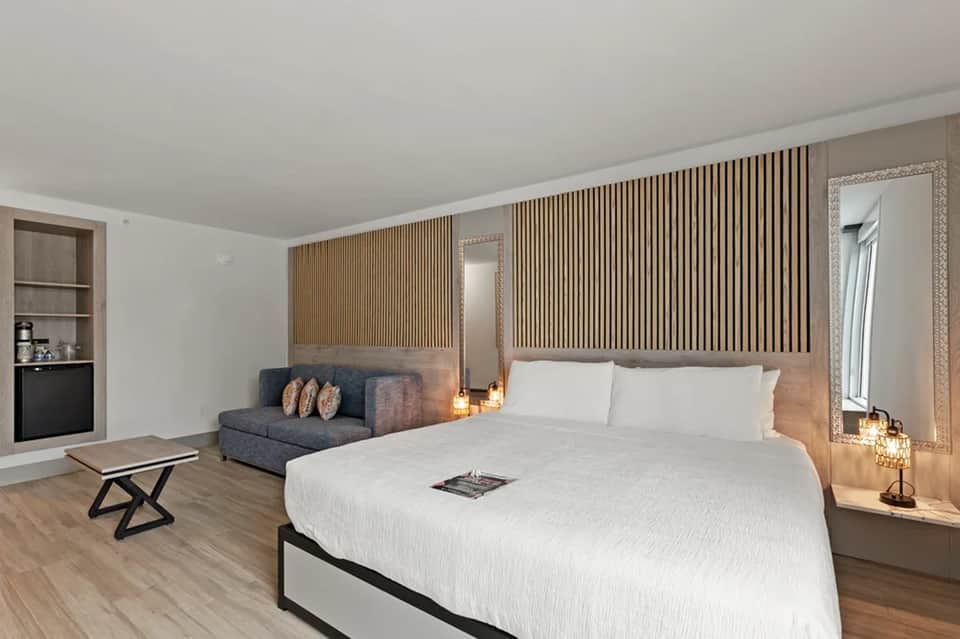 Modern hotel room with king bed, sofa, wooden wall panels, and contemporary minimalist design