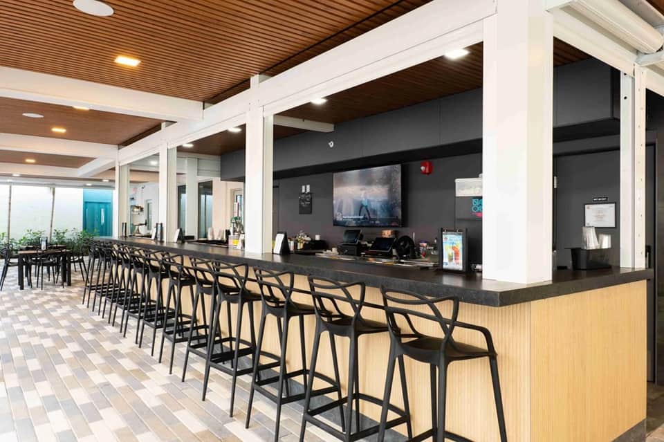 Resort bar counter with black chairs, wooden ceiling, TV screen, and modern lounge area design