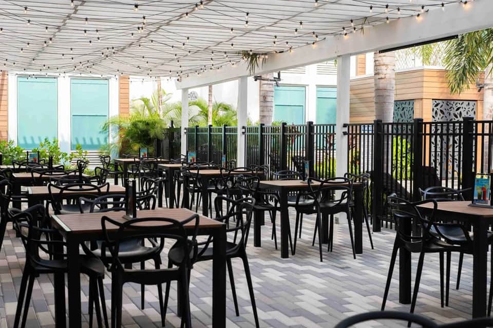 Covered outdoor dining area with black tables and chairs, string lights, and waterfront views