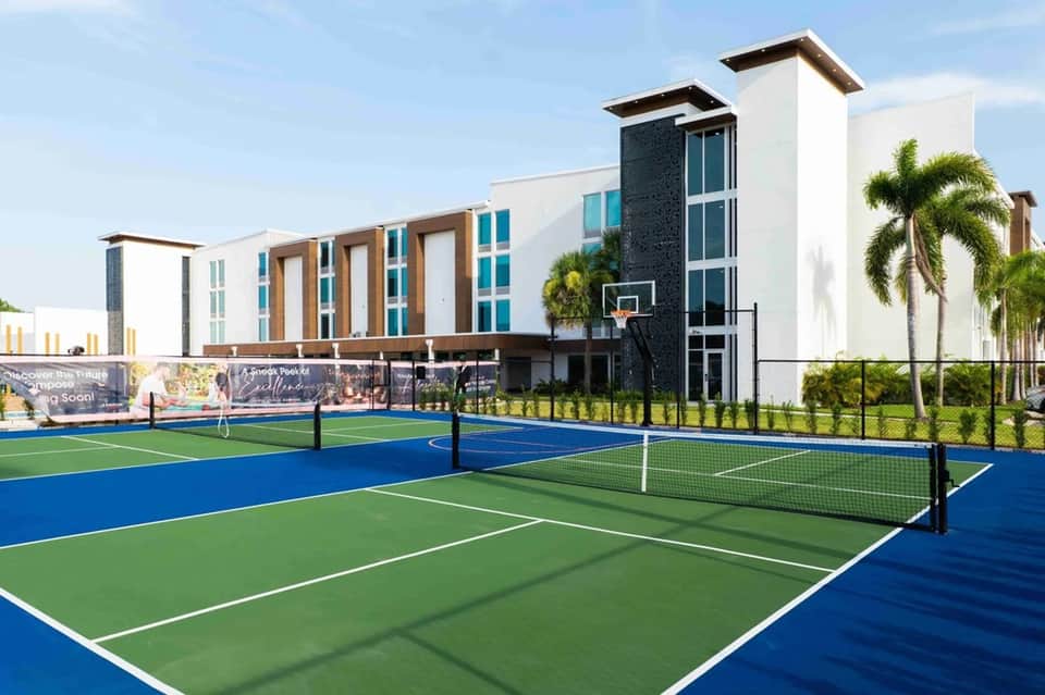 Modern resort with pickleball courts, contemporary white and teal building with palm trees visible
