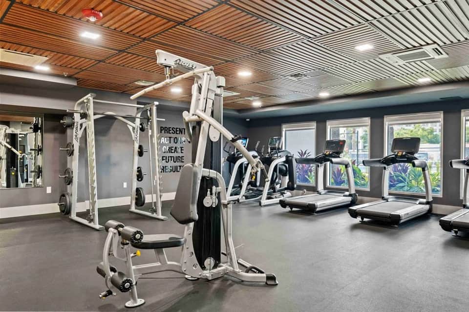 Modern fitness center with cardio equipment, weight machines, wood ceiling, and glass doors