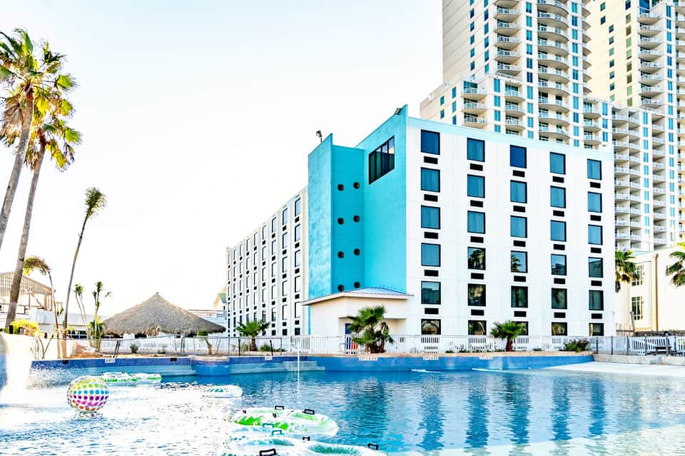 Bright blue modern hotel buildings with pool and palm trees in coastal resort setting
