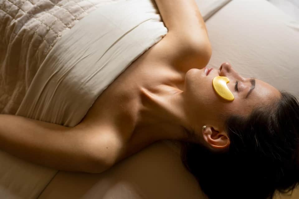 Woman relaxing on bed during spa treatment with yellow eye pads