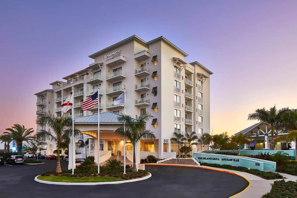 Residential hotel building at dusk with flags, palm trees, and entry portico