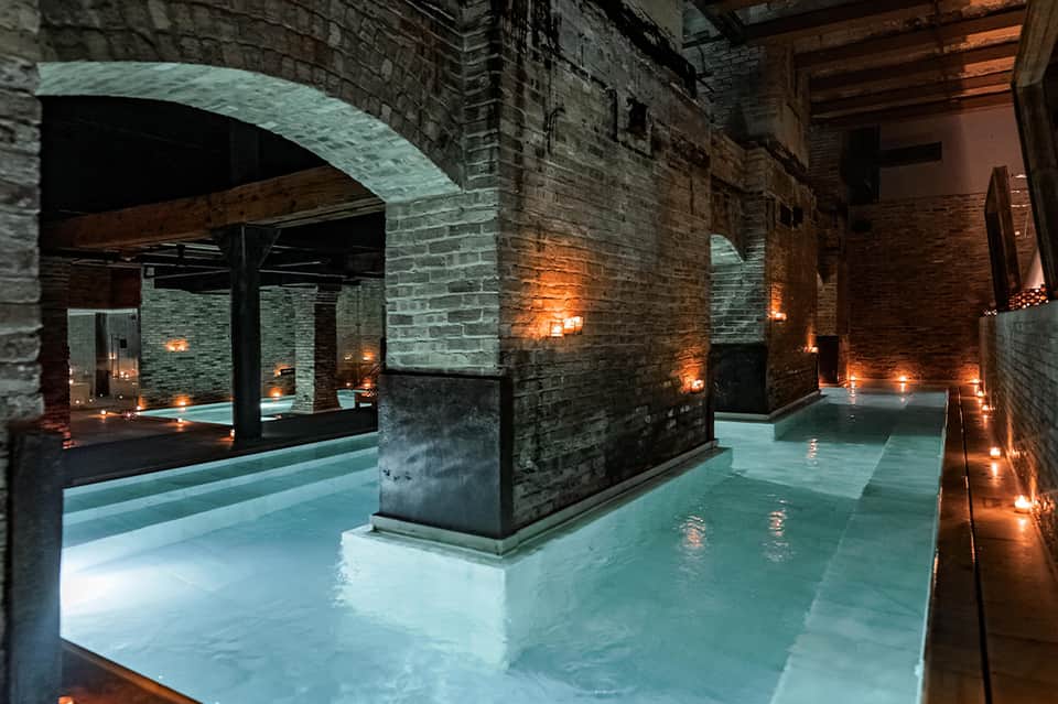 Underground spa or pool area with brick arches, ambient lighting, and illuminated water features