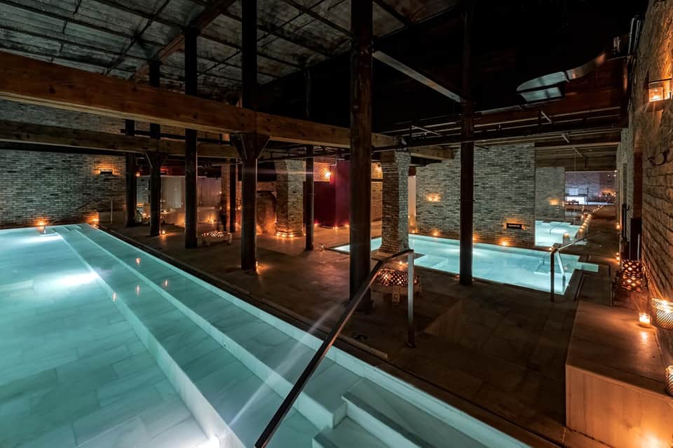 Indoor lap pool facility at night with ambient lighting, exposed beams, and brick architecture