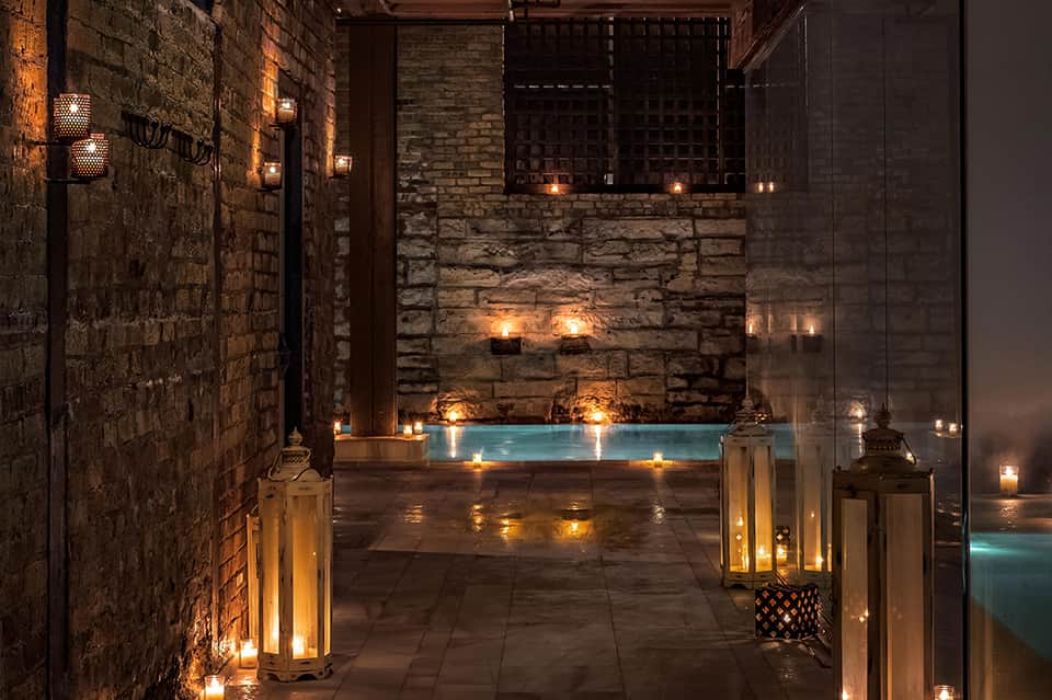 Luxurious spa courtyard with illuminated indoor pool surrounded by stone walls and ambient candlelight