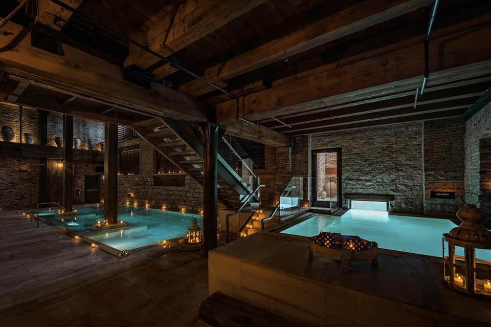 Luxurious spa with twin heated pools, brick walls, wooden beams, and ambient candlelight