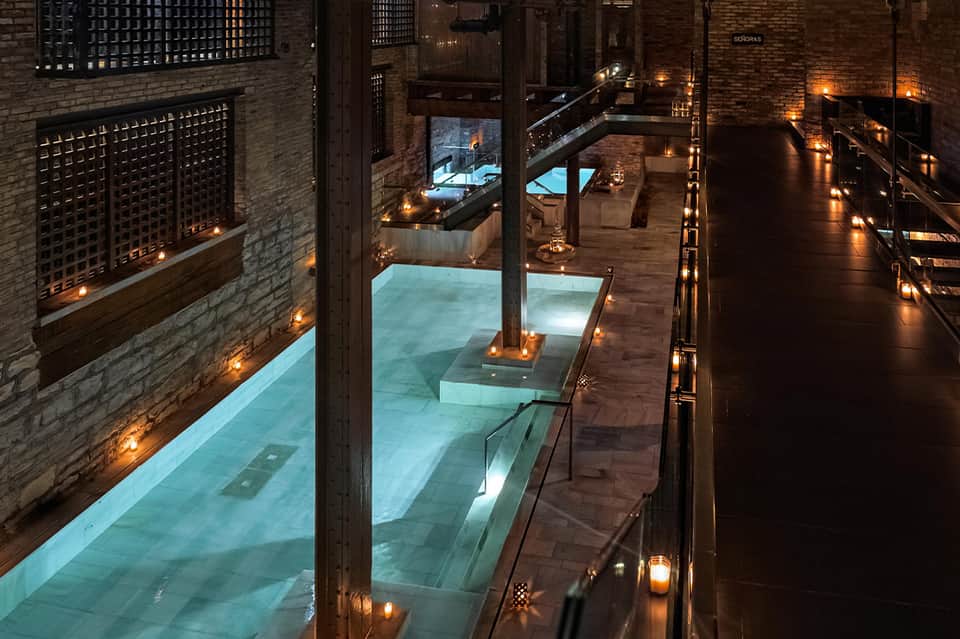 Nighttime courtyard view of illuminated indoor pools and wooden walkways