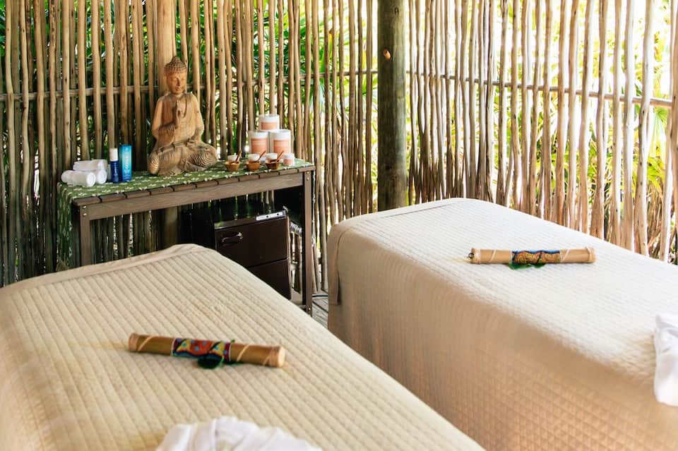 Spa treatment room with two massage tables, bamboo walls, Buddha statue, and zen garden décor