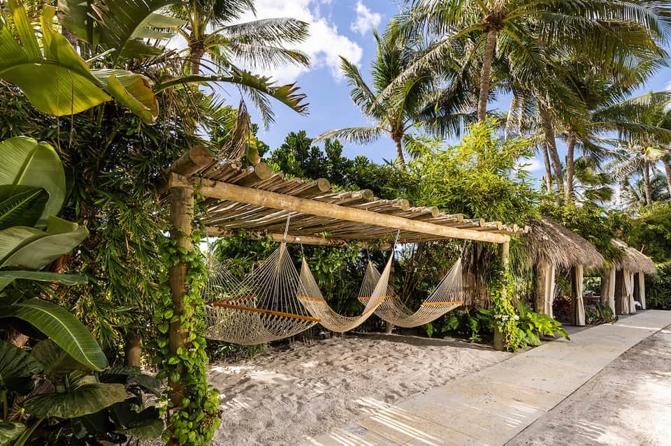 Tropical beach resort with hammocks under wooden pergola, palm trees, and thatched structures