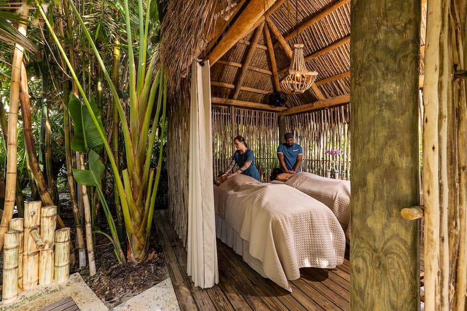 Outdoor spa massage pavilion with thatched roof, tropical plants, and two massage beds