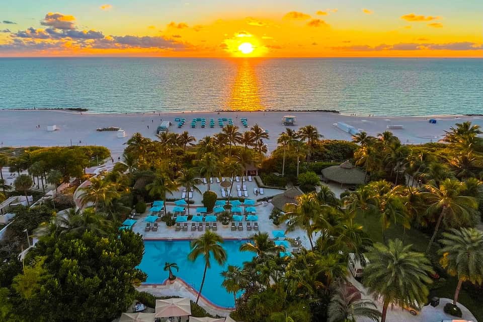 Beachfront resort at golden sunset with turquoise pool, palm trees, sandy beach, and calm ocean