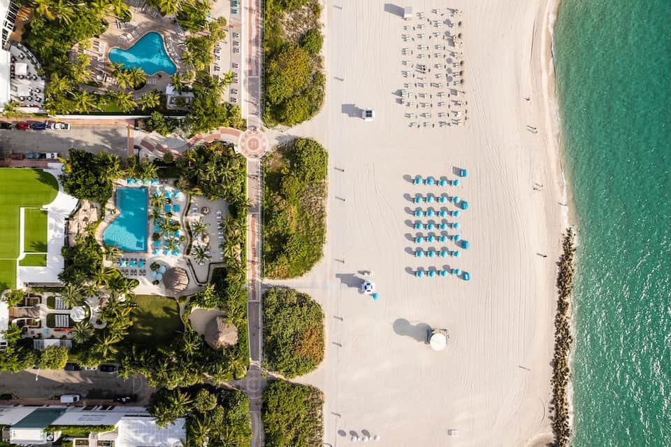 Aerial view of beachfront resort with pool, building, beach umbrellas, and turquoise ocean