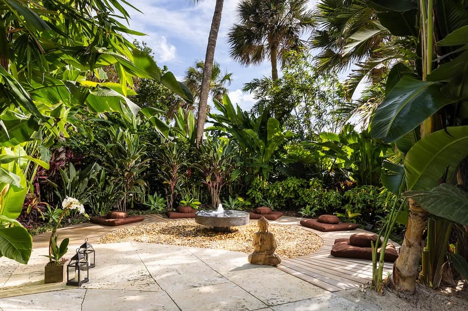 Tropical garden patio with stone pathways, palm trees, and zen water feature