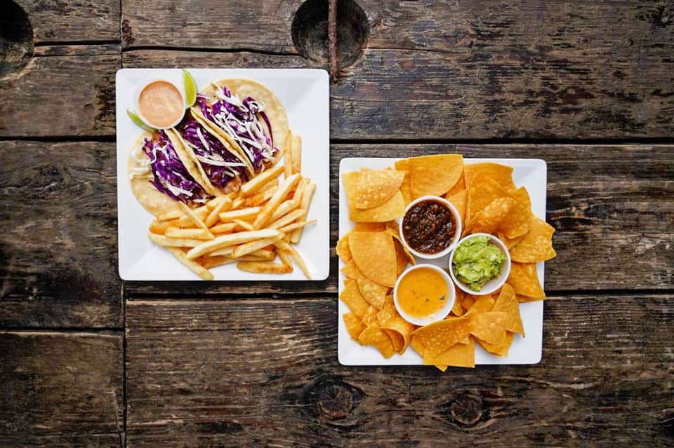 Tacos with purple cabbage and fries, and tortilla chips with salsa and guacamole on wooden table