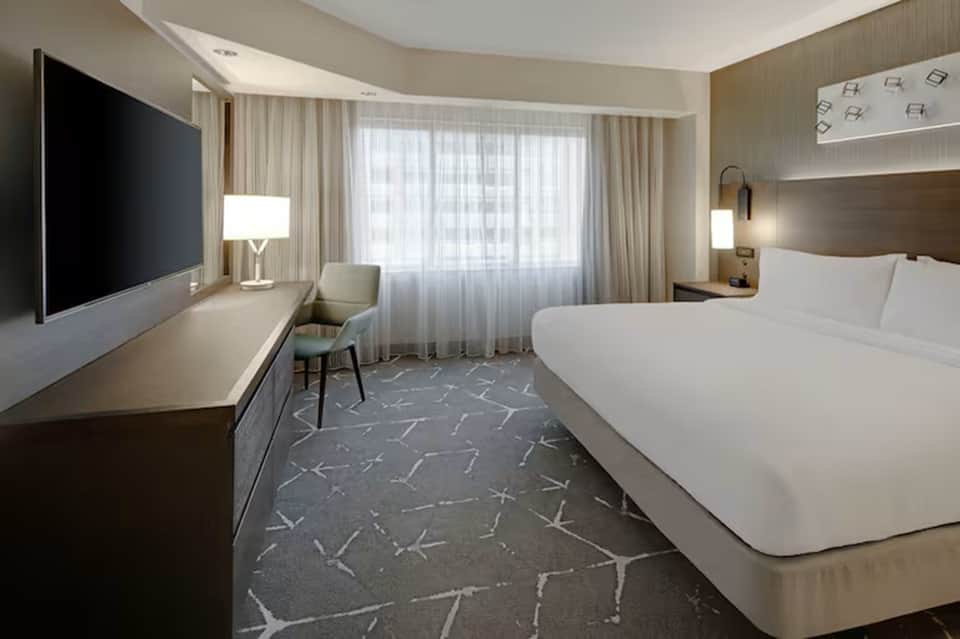 Contemporary hotel room with queen bed, flat-screen TV, desk, and floor-to-ceiling windows