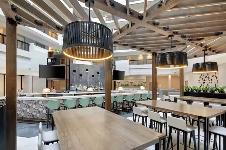 Modern hotel restaurant interior with pendant lighting, bar counter, and dining tables under geometric ceiling