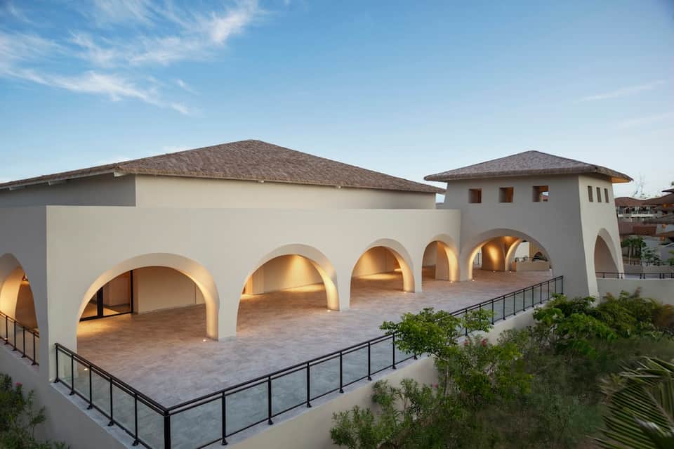Contemporary white building with arched colonnade, travertine terrace, and dramatic lighting at dusk