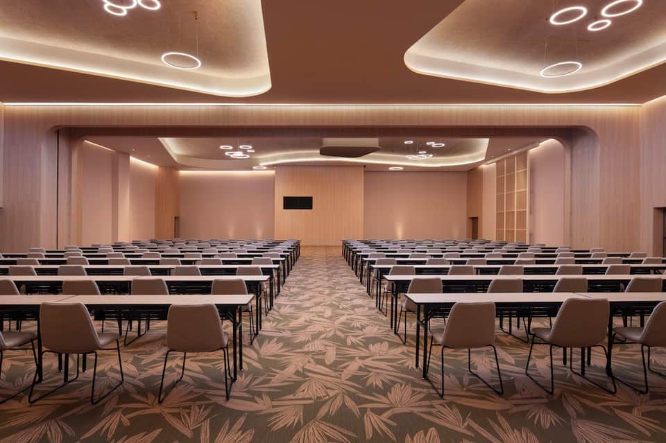 Large conference room with theater-style seating, modern ceiling lighting, and neutral décor
