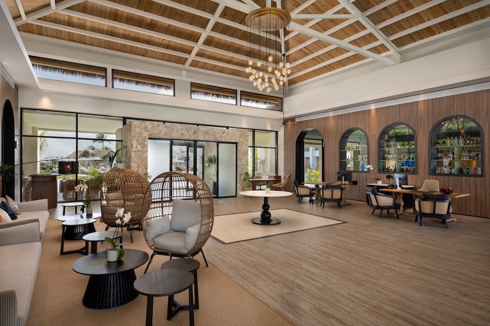 Elegant resort lobby with pendant chandelier, woven chair seating, bar, and high wood-beam ceiling