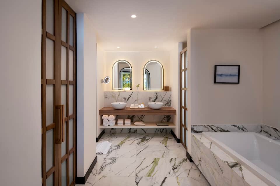 Modern bathroom with dual vessel sinks, marble countertop, arched mirrors, and soaking tub