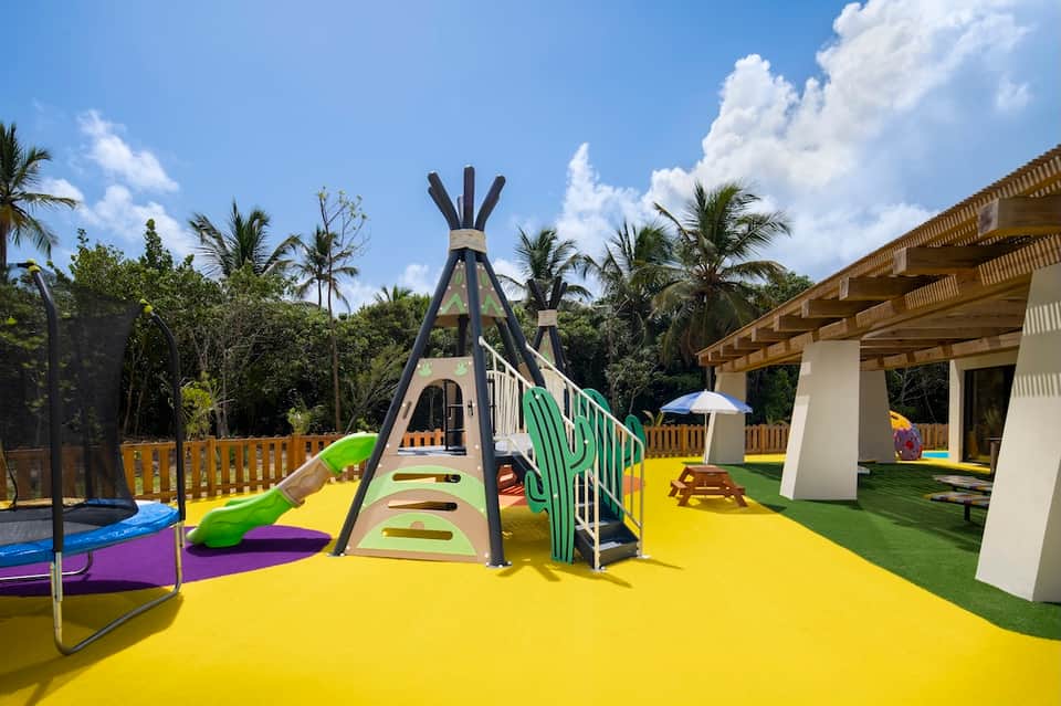 Colorful children's playground with slide, teepee structure, and palm trees