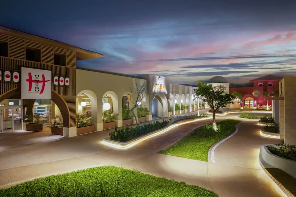 Modern indoor shopping promenade with arched architecture, colorful storefronts, illuminated pathways, and evening sky