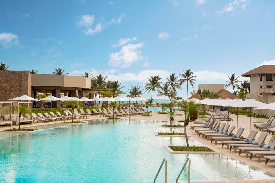Expansive resort pool surrounded by loungers, umbrellas, and beachfront buildings