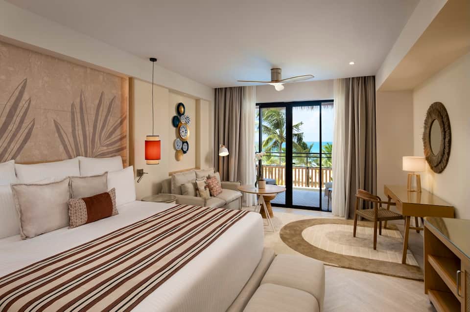 Beachfront hotel bedroom with ocean view, balcony, tropical decor, and modern furnishings