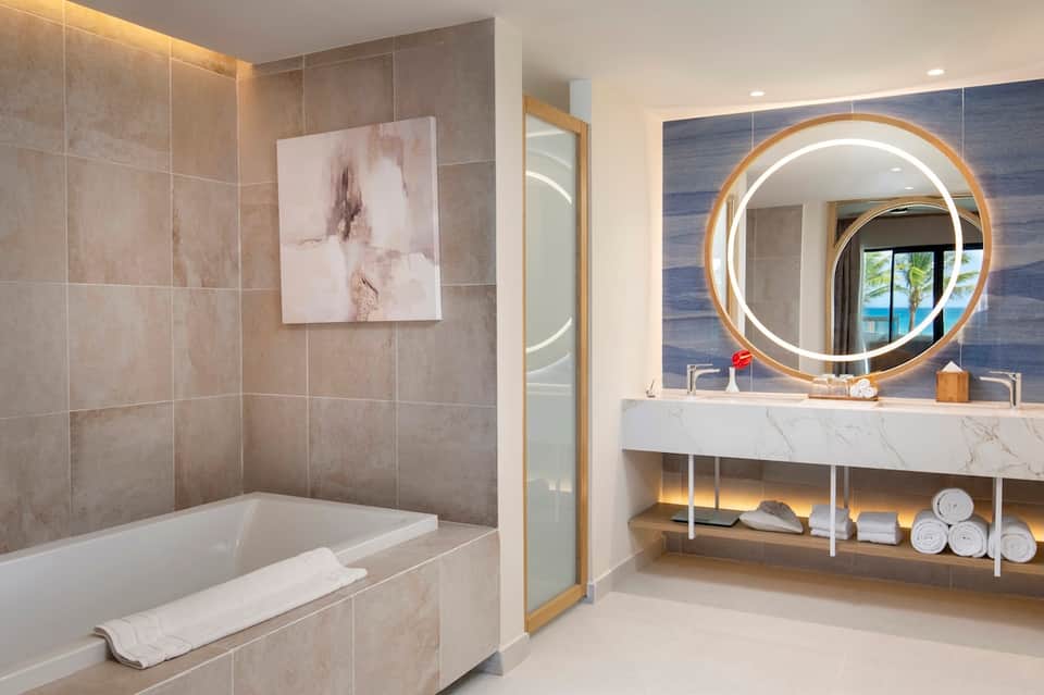 Luxury bathroom with marble tile, soaking tub, illuminated round mirror, and ocean view