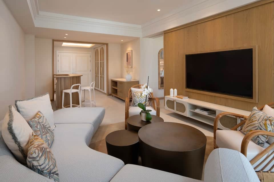 Modern hotel suite living room with white sofa, wooden accents, and flat-screen TV