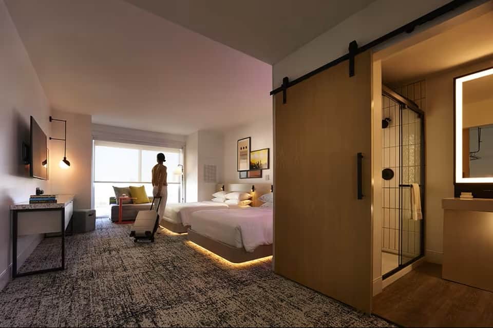 Modern hotel bedroom with king bed, ensuite bathroom with glass shower, and contemporary furnishings