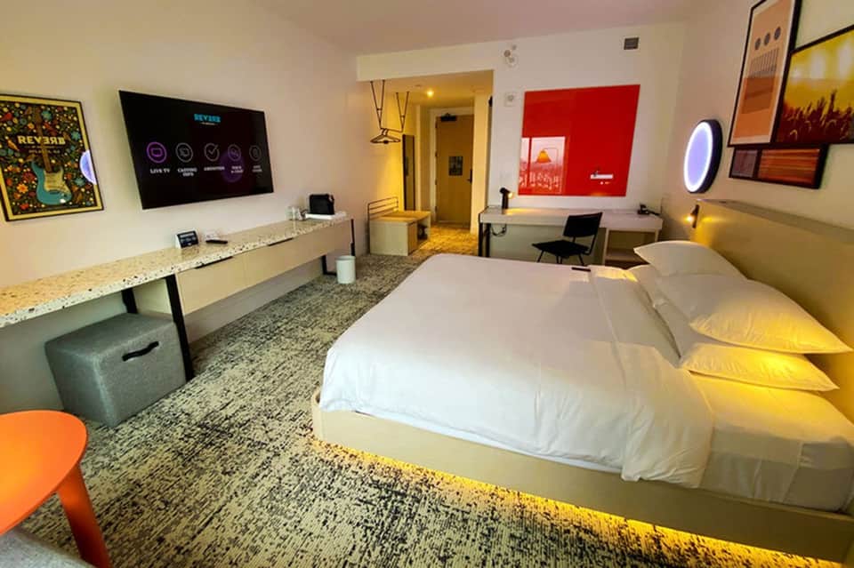 Contemporary hotel room with queen bed, desk area, accent lighting, and entertainment system