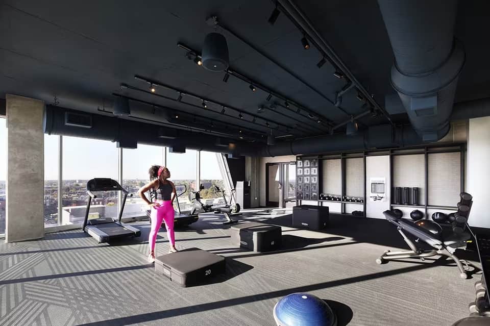 High-rise gym with floor-to-ceiling windows, city views, treadmill, and exercise equipment