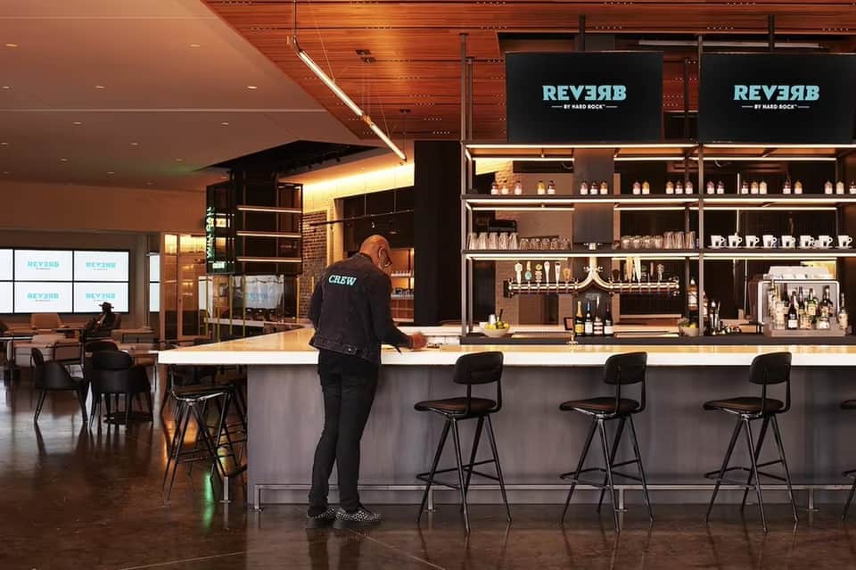 Modern bar interior with staff member at counter, illuminated shelving displaying bottles, and dark wood accents