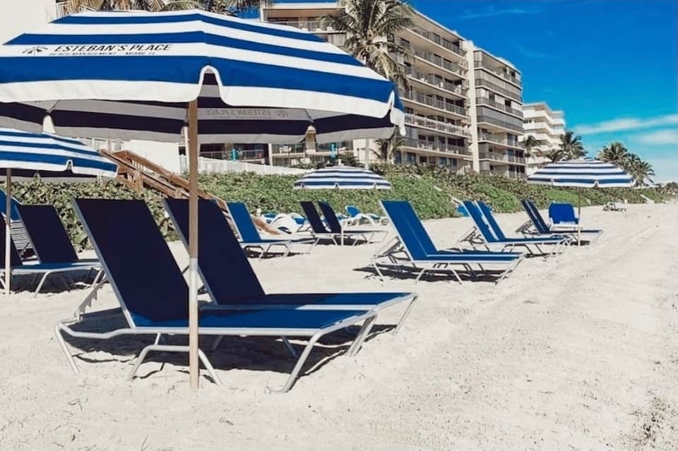 Beach with blue and white striped umbrellas, lounge chairs, beachfront condominiums, and ocean