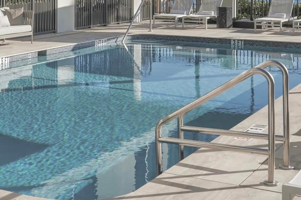 Contemporary outdoor pool with mosaic tile waterline, metal railings, and lounging area