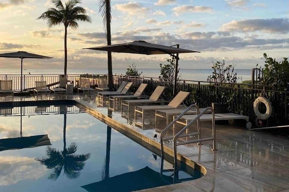 Oceanfront resort infinity pool at sunset with lounge chairs, umbrellas, and tropical coastal views