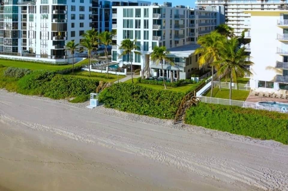 Beachfront resort buildings with manicured landscaping, palm trees, and sandy beach access