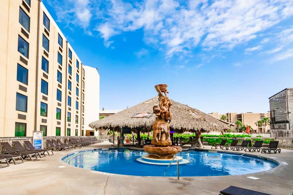 Resort pool with wooden tiki-style centerpiece sculpture and lounge chairs on sunny deck