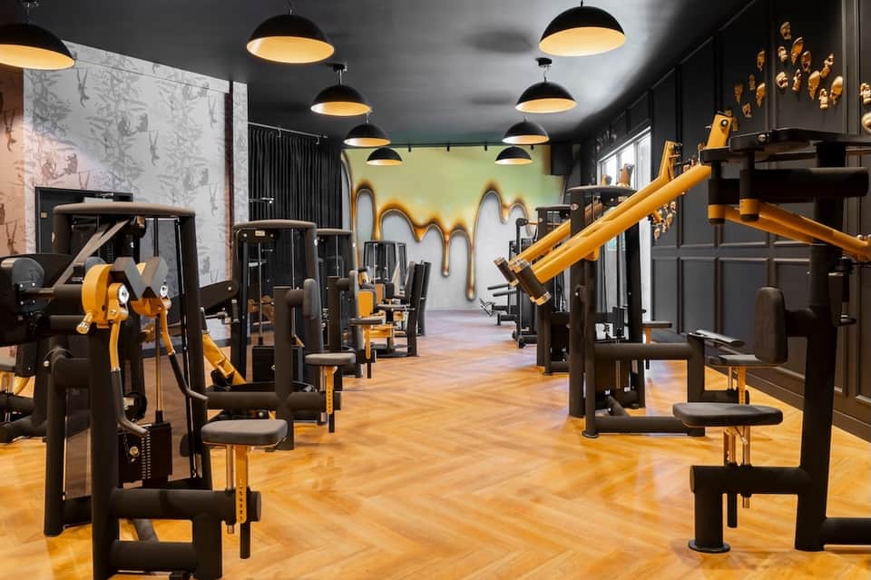 Modern fitness center with black exercise equipment, yellow accents, pendant lighting, and artistic wall