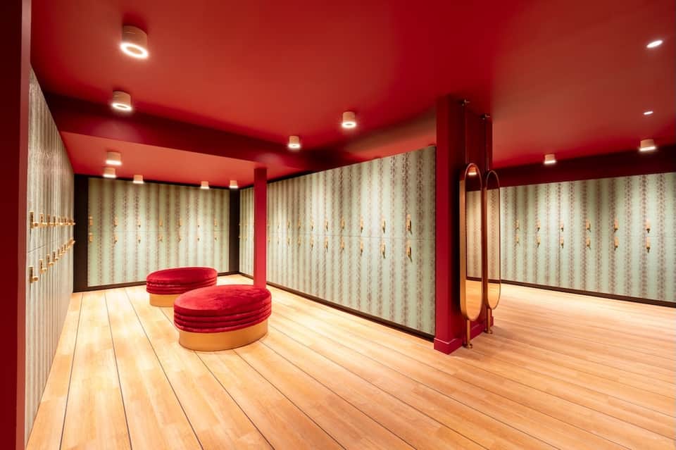 Spa dressing room with bold red ceiling, cream-colored lockers, and wooden circular seating