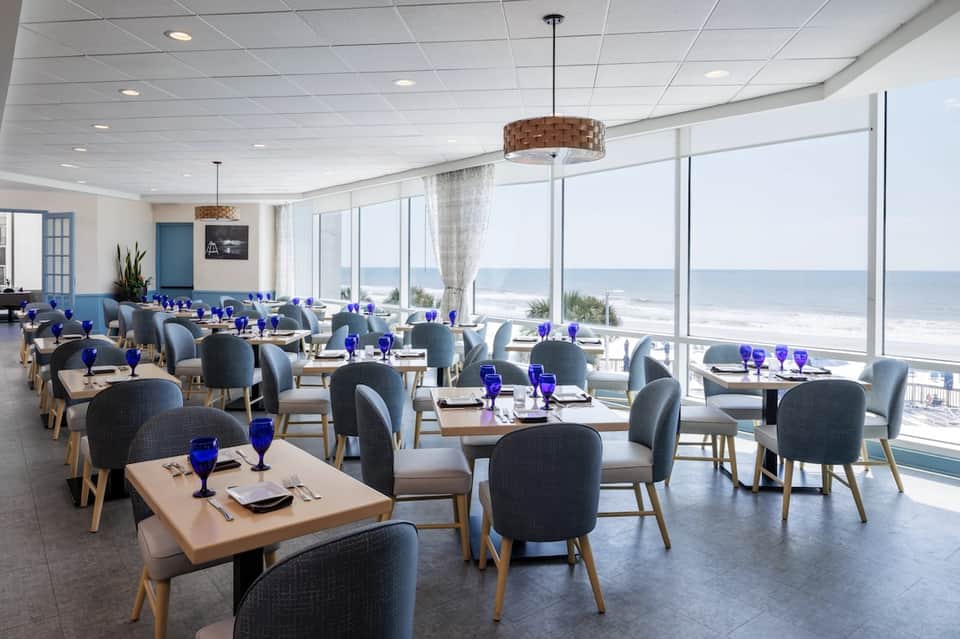 Beachfront dining room with ocean views, blue glassware, and floor-to-ceiling windows