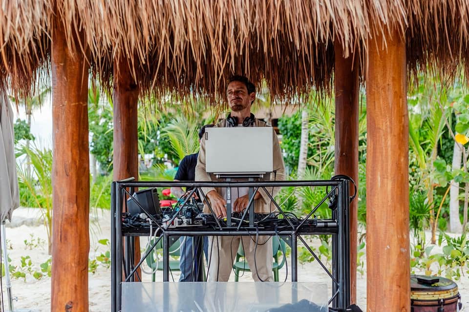 Man working at laptop under thatched roof pavilion in tropical garden setting